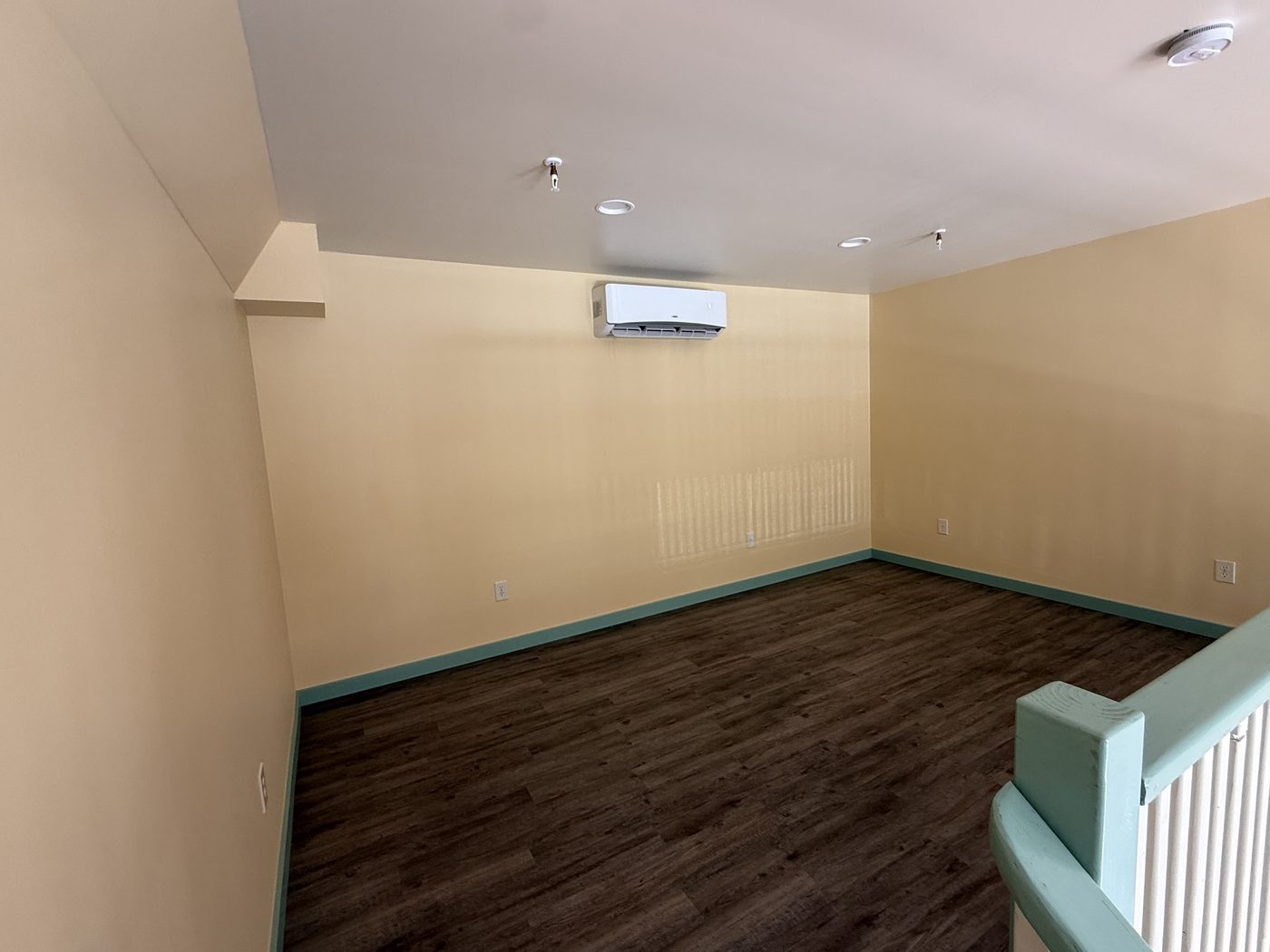 The Crown loft room — yellow walls, mint railing, wood floor (furnishing in progress)